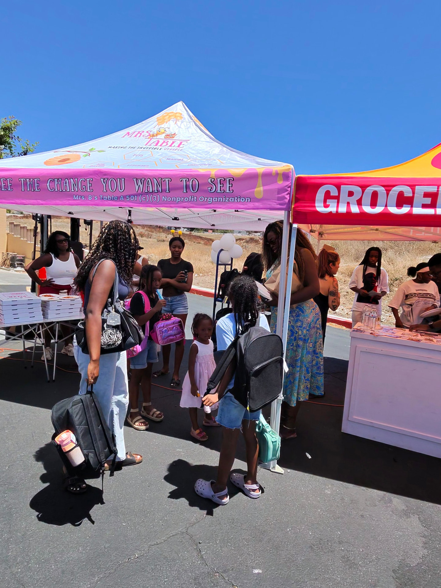 Families with backpacks gather beneath the Mrs. B’s Table tent at Grocery Outlet.